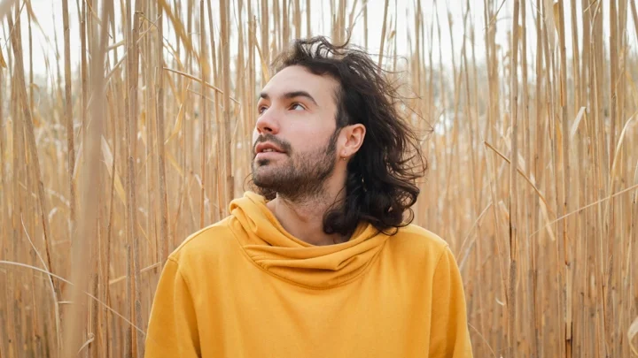 Photo montrant la photographe inclusive Ken Lecoq, vêtue de jaune sur un fond de tiges de plantes, près de Nantes et St-Pazanne.