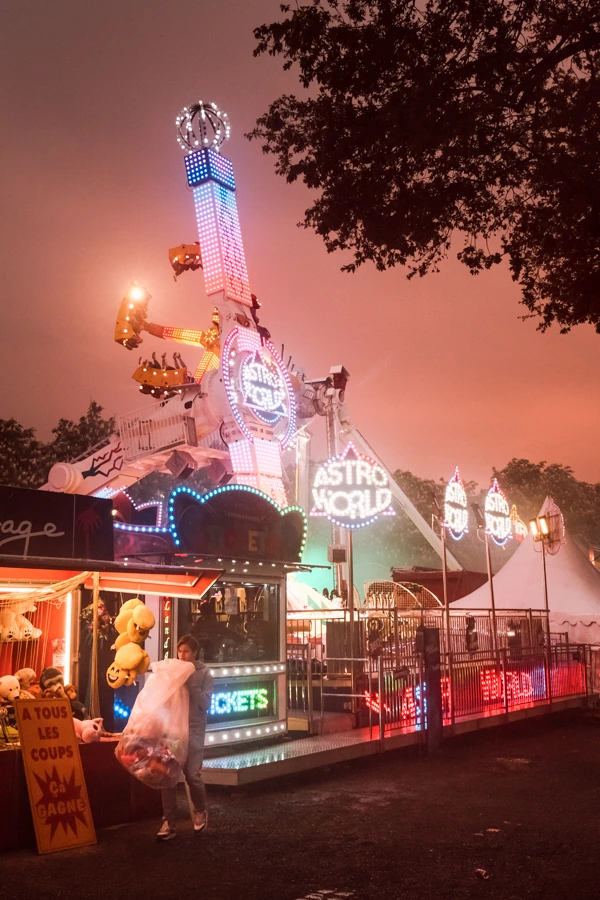 Photo de fête foraine montrant des manèges et des boutiques avec un garçon tenant un sac, à Nantes, par un photographe professionnel.